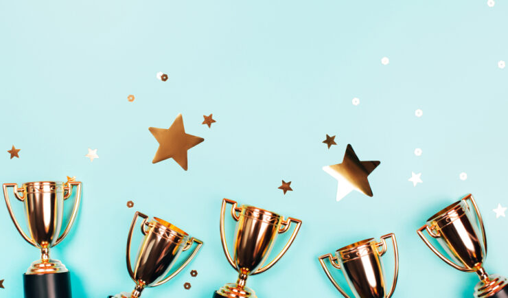 Golden cups of winner with shiny confetti on a blue background with copy space. Flat lay style.